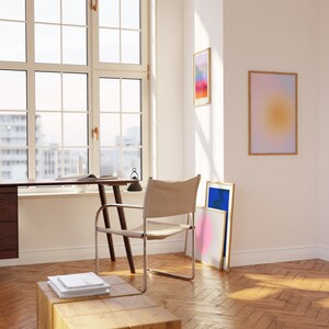 May include: A light wood desk with a white chair and a lamp. There are three framed abstract art prints on the wall behind the desk. The room has hardwood floors.