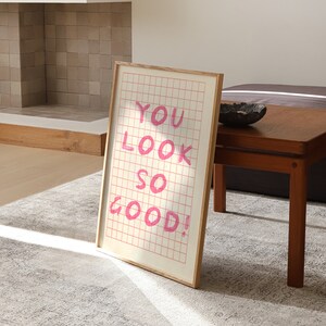 K&ouml;nnte beinhalten: Ein gerahmter Druck mit einem rosa Gittermuster und dem Text "YOU LOOK SO GOOD!" in rosa Schrift.