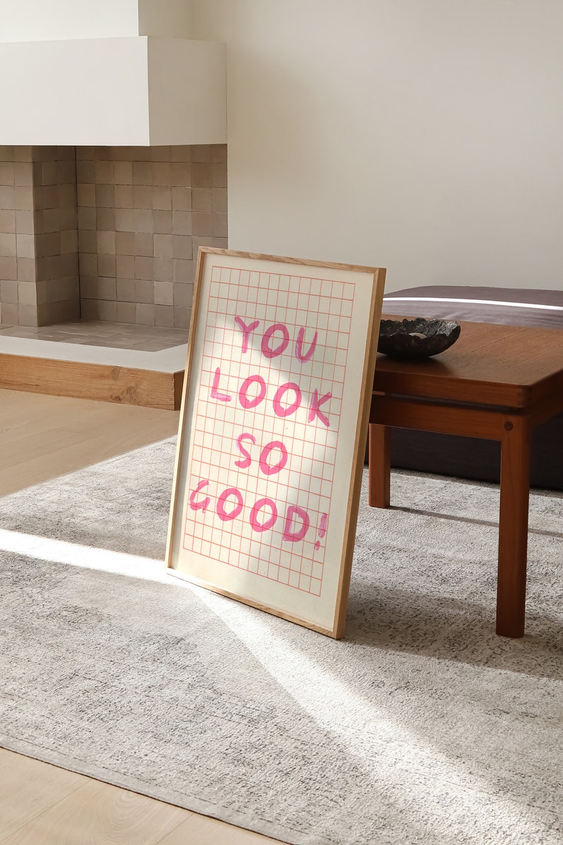K&ouml;nnte beinhalten: Ein gerahmter Druck mit einem rosa Gittermuster und dem Text "YOU LOOK SO GOOD!" in rosa Schrift.