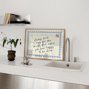 May include: A framed postcard print with a light blue border and the words "always find time for the things that make you feel happy to be alive." A small potted plant and a silver teapot are on the counter.