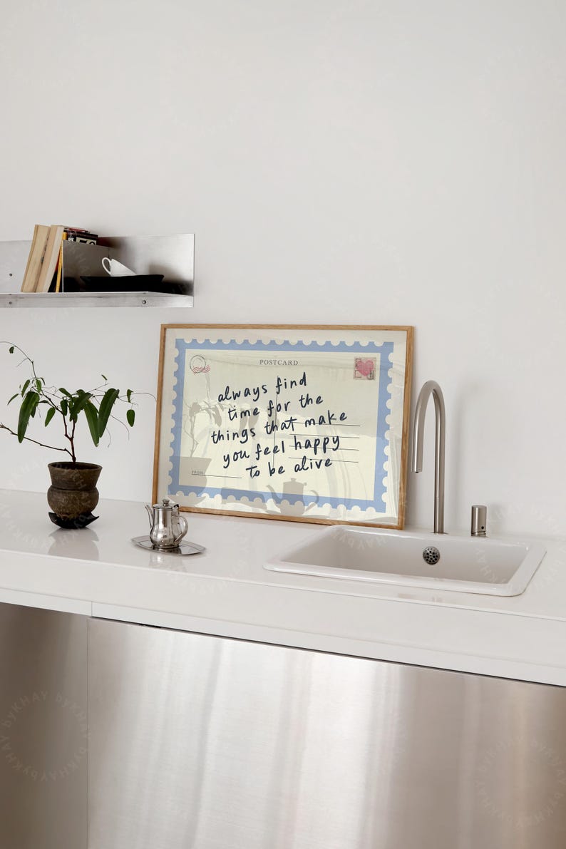 May include: A framed postcard print with a light blue border and the words "always find time for the things that make you feel happy to be alive." A small potted plant and a silver teapot are on the counter.