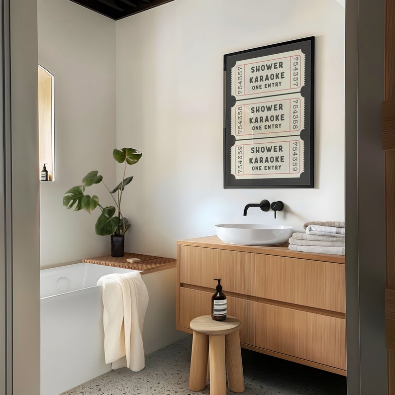 May include: A bathroom with a white bathtub, a wooden vanity with a white sink, and a framed print of three tickets that say "Shower Karaoke One Entry".