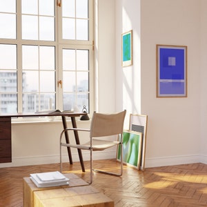 May include: A light wood desk with a chair and a window in the background. There are three framed abstract art prints on the wall.