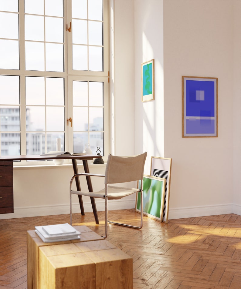 May include: A light wood desk with a chair and a window in the background. There are three framed abstract art prints on the wall.