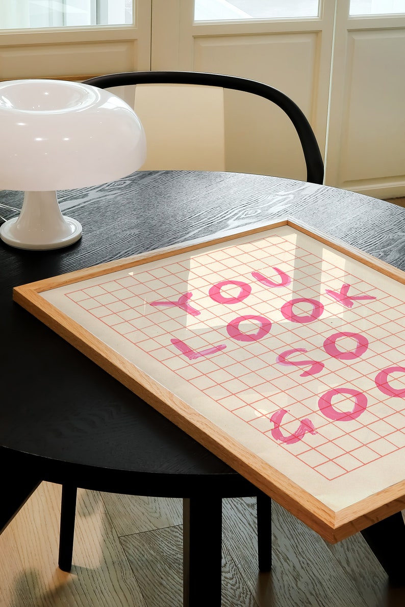K&ouml;nnte beinhalten: Ein gerahmter Druck mit einem rosa Gittermuster und dem Text "YOU LOOK SO GOOD" in rosa.