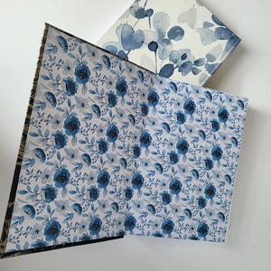 Puede incluir: Dos cuadernos abiertos con diseños florales. Uno presenta un patrón de rosas azules y pequeñas flores blancas sobre un fondo claro. El otro tiene un diseño de hojas de eucalipto azules sobre un fondo blanco.