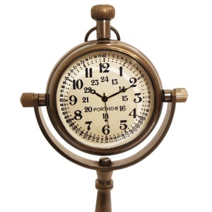 K&ouml;nnte beinhalten: Eine antike Messing-Uhr mit einem runden Zifferblatt und schwarzen Zeigern. Die Uhr hat einen Standfu&szlig; mit einem runden Sockel und einem langen, d&uuml;nnen Stiel. Das Zifferblatt der Uhr hat r&ouml;mische Ziffern und eine 24-Stunden-Zeitskala.