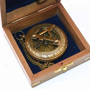 Può includere: Una bussola in ottone con una catena in una scatola di legno con fodera in velluto blu. La bussola ha una rosa dei venti e una meridiana.