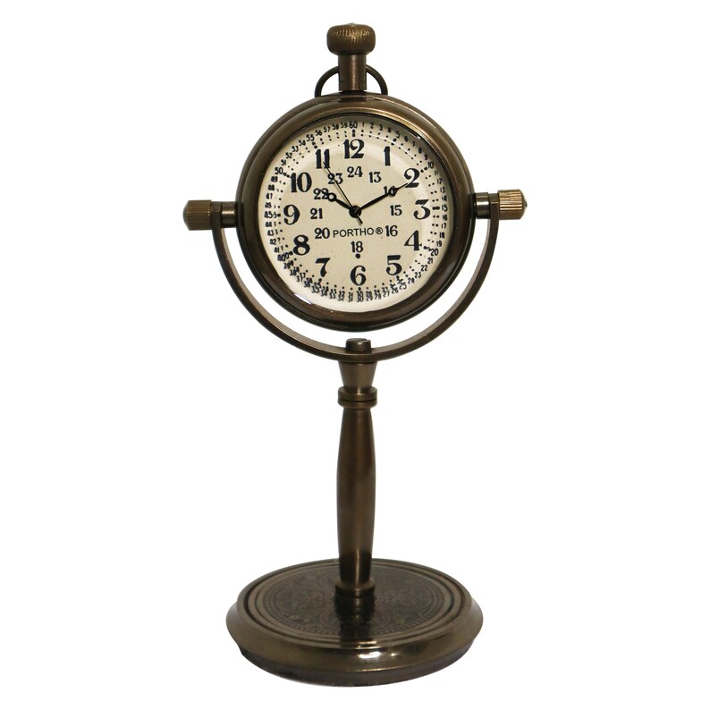 K&ouml;nnte beinhalten: Eine Messing-Tischuhr mit einem runden Zifferblatt und einem St&auml;nder. Das Zifferblatt der Uhr hat schwarze Zahlen und einen wei&szlig;en Hintergrund. Der St&auml;nder ist eine runde Basis mit einer hohen, zylindrischen S&auml;ule.