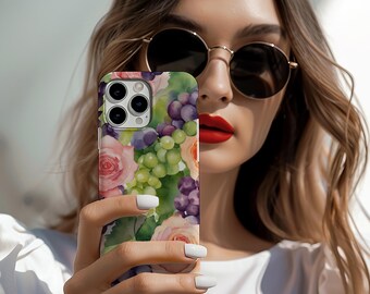 May include: A smartphone case featuring a watercolor design of pink roses, green and purple grapes, and green leaves. The case has a glossy finish and a camera cutout. The case is held in front of a person wearing sunglasses and a white shirt.