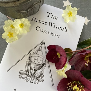 May include: A white book with black text that reads "The Hedge Witch's Cauldron" and "Rachael Coats". The book features a black and white illustration of a cauldron hanging over a fire.