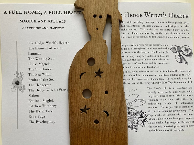 May include: A wooden cutout of a witch's house with a crescent moon, star, and sun cutouts. The text "Hedge Witch's Hearth" is printed on the page next to the cutout.