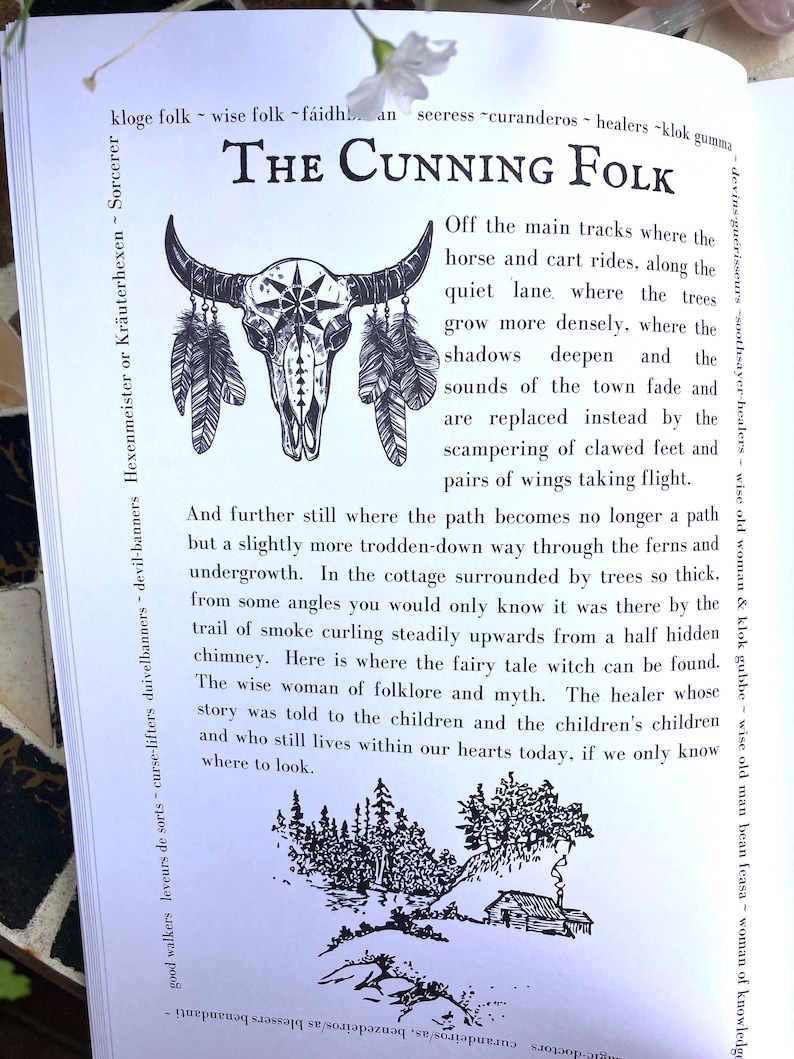 May include: Black and white illustration of a skull with feathers and a cottage in a forest. The text "The Cunning Folk" is at the top of the image. The text below the image reads "And further still where the path becomes no longer a path but a slightly more trodden-down way through the ferns and undergrowth. In the cottage surrounded by trees so thick, from some angles you would only know it was there by the trail of smoke curling steadily upwards from a half hidden chimney. Here is where the fairy tale witch can be found. The wise woman of folklore and myth. The healer whose story was told to the children and the children's children and who still lives within our hearts today, if we only know where to look."