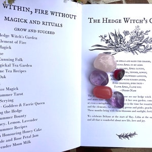 May include: An open book with the title "The Hedge Witch's Garden" and a list of rituals and magick for each month of the year.  The book is open to the page for April and features five colorful gemstones: pink, purple, red, and two shades of amethyst.