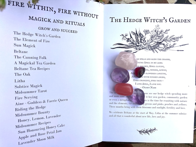 May include: An open book with the title "The Hedge Witch's Garden" and a list of rituals and magick for each month of the year.  The book is open to the page for April and features five colorful gemstones: pink, purple, red, and two shades of amethyst.