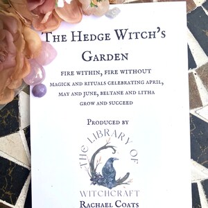 May include: A white card with black text that reads "The Hedge Witch's Garden Fire Within, Fire Without Magick and Rituals Celebrating April, May and June, Beltane and Litha Grow and Succeed" and a black and white illustration of a raven on a branch with the text "The Library of Witchcraft Rachael Coats" below.