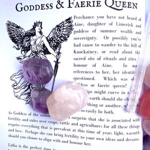 May include: Aine, Goddess & Faerie Queen, a black and white illustration of a winged woman holding a sword. Text on the page describes Aine as a goddess of summer wealth and sovereignty. The image also includes several colorful crystals.