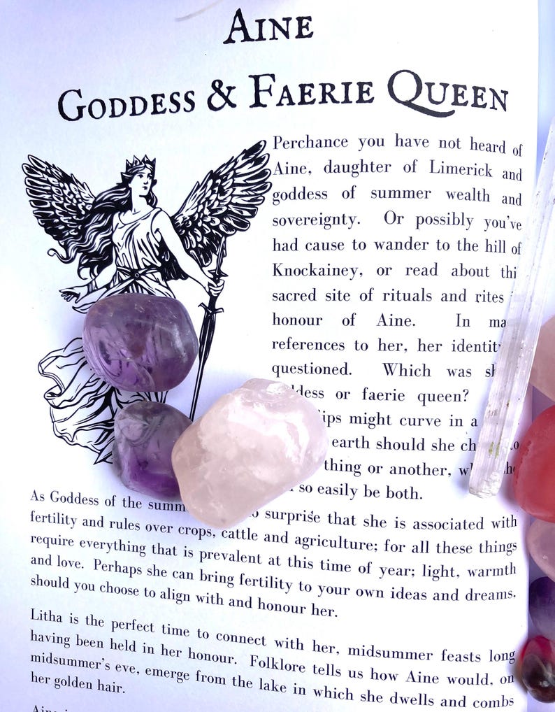 May include: Aine, Goddess & Faerie Queen, a black and white illustration of a winged woman holding a sword. Text on the page describes Aine as a goddess of summer wealth and sovereignty. The image also includes several colorful crystals.