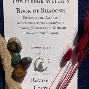 May include: A white book with the title "The Hedge Witch's Book of Shadows: Entering the Darkness, Magick and Rituals Celebrating October, November and Samhain, Embracing the Shadow." The book is produced by "The Library of Witchcraft" by Rachael Coats.