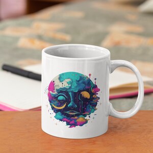 Puede incluir: Taza de cer&aacute;mica blanca con una ilustraci&oacute;n colorida de una cara rodeada de nubes y estrellas. La cara tiene un esquema de color azul y verde con acentos amarillos.