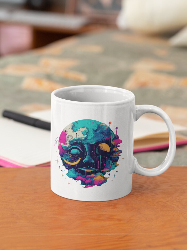 Puede incluir: Taza de cer&aacute;mica blanca con una ilustraci&oacute;n colorida de una cara rodeada de nubes y estrellas. La cara tiene un esquema de color azul y verde con acentos amarillos.