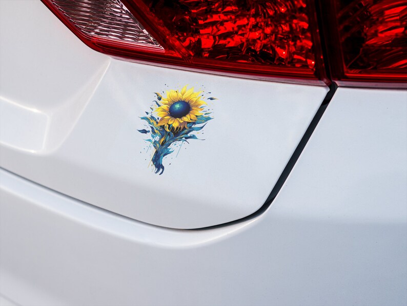 K&ouml;nnte beinhalten: Ein wei&szlig;es Auto mit einem blauen und gelben Sonnenblumen-Aufkleber auf der hinteren Sto&szlig;stange.