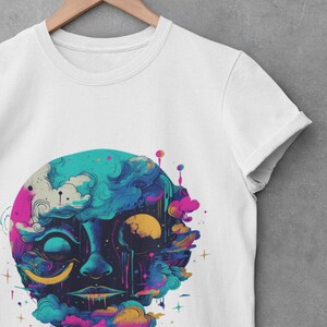 Puede incluir: Camiseta blanca con un estampado gr&aacute;fico colorido de una cara rodeada de nubes y estrellas. La cara est&aacute; compuesta por colores azules, rosas, amarillos y morados.