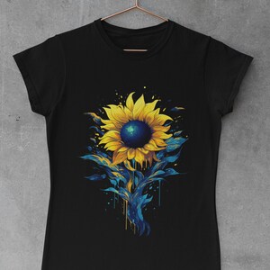 K&ouml;nnte beinhalten: Schwarzes T-Shirt mit einem bunten Sonnenblumen-Motiv. Die Sonnenblume ist in Gelb-, Blau- und Gr&uuml;nt&ouml;nen bemalt, mit Farbtropfen, die den Stiel hinunterlaufen.