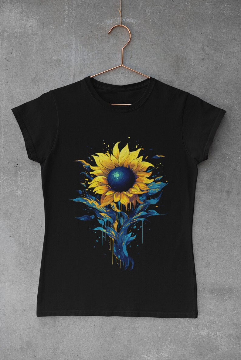 K&ouml;nnte beinhalten: Schwarzes T-Shirt mit einem bunten Sonnenblumen-Motiv. Die Sonnenblume ist in Gelb-, Blau- und Gr&uuml;nt&ouml;nen bemalt, mit Farbtropfen, die den Stiel hinunterlaufen.