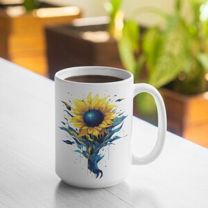 K&ouml;nnte beinhalten: Wei&szlig;e Keramiktasse mit einem blauen und gelben Sonnenblumen-Design. Die Sonnenblume hat eine dunkelblaue Mitte und gelbe Bl&uuml;tenbl&auml;tter. Die Tasse ist mit Kaffee gef&uuml;llt.