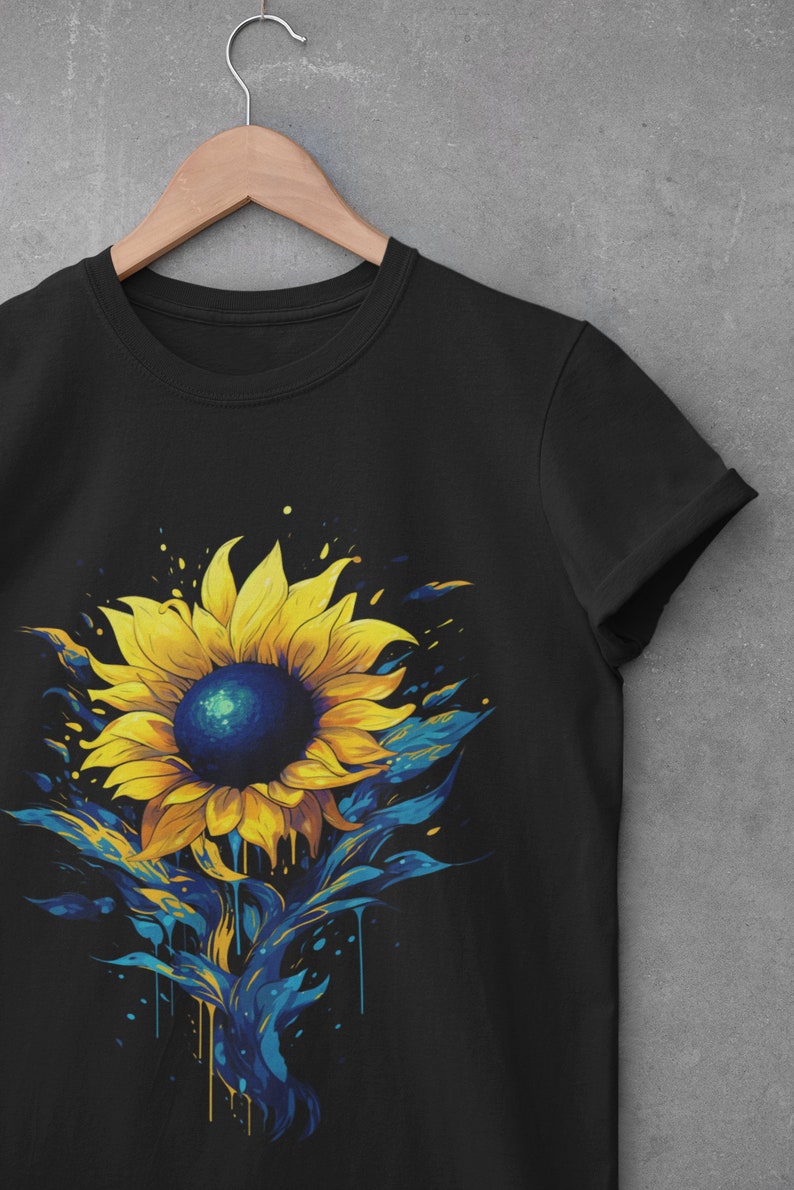 K&ouml;nnte beinhalten: Schwarzes T-Shirt mit einem bunten Grafikdruck eines Sonnenblumenmotivs mit blauen und gelben Farbstichen.