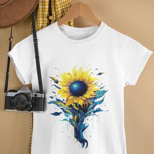 K&ouml;nnte beinhalten: Wei&szlig;es T-Shirt mit einem blauen und gelben Sonnenblumen-Motiv. Die Sonnenblume hat eine blaue Mitte und gelbe Bl&uuml;tenbl&auml;tter mit blauen Farbstichen.