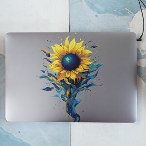 K&ouml;nnte beinhalten: Ein silberner Laptop mit einem Aufkleber eines gelben Sonnenblumen mit einem blauen Zentrum und blauen und gr&uuml;nen aquarellartigen Details auf der R&uuml;ckseite.