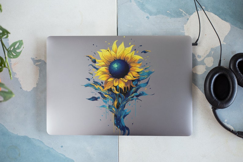 K&ouml;nnte beinhalten: Ein silberner Laptop mit einem Aufkleber eines gelben Sonnenblumen mit einem blauen Zentrum und blauen und gr&uuml;nen aquarellartigen Details auf der R&uuml;ckseite.