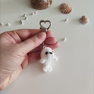 May include: White crocheted seal keyring with black eyes. The keyring has a silver heart-shaped clasp.