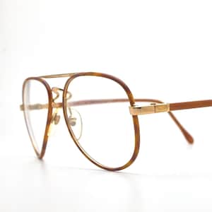 May include: Aviator-style spectacles featuring a brown tortoiseshell pattern frame with gold-tone metal accents. The glasses include a double bridge design, clear lenses, and thin, straight temples that extend from the gold-tone hinges.
