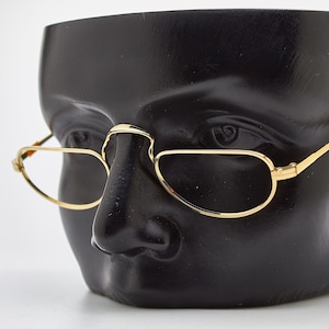 Puede incluir: Gafas ovaladas con montura dorada en una cabeza de maniquí negra.