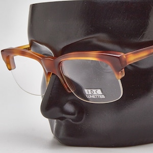 May include: Tortoise shell eyeglasses with clear lenses. The glasses are on a black mannequin head. The brand name "IDC Lunettes" is printed on the frame.