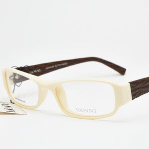 May include: Cream-coloured rectangular eyeglasses with textured dark brown arms. The brand name "VANNI" is visible on the frame and a tag. The glasses have a contemporary design and are set against a white background.