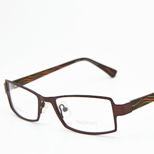 May include: Dark brown rectangular eyeglasses with a decorative wave pattern in red, green, and yellow on the arms. The brand name "VANNI" is visible on the lens. The frames are a dark brown colour.