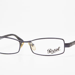 Puede incluir: Un par de gafas Persol con montura rectangular azul oscuro. Las patillas y la montura son de color azul oscuro. El logotipo de Persol está impreso en la lente derecha.