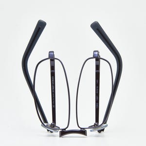 Puede incluir: Gafas Giorgio Armani negras con montura rectangular y patillas curvas. Las gafas tienen un diseño minimalista con el nombre de la marca impreso en las patillas. La montura es de un material oscuro, posiblemente metálico.
