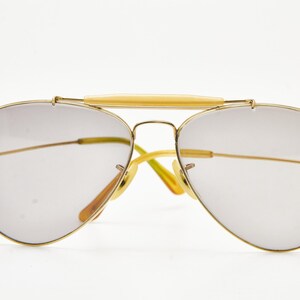 Puede incluir: Gafas de sol estilo aviador con montura de metal dorado y lentes gris claro. El puente y las patillas tienen un acento amarillo claro. Las lentes tienen forma de l&aacute;grima y el dise&ntilde;o es cl&aacute;sico y elegante.