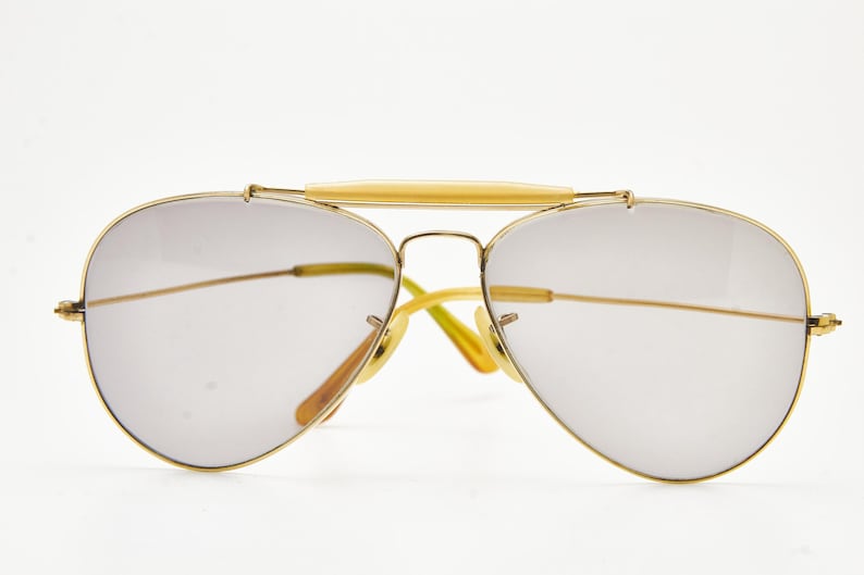 Puede incluir: Gafas de sol estilo aviador con montura de metal dorado y lentes gris claro. El puente y las patillas tienen un acento amarillo claro. Las lentes tienen forma de l&aacute;grima y el dise&ntilde;o es cl&aacute;sico y elegante.