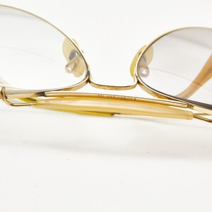 Puede incluir: Primer plano de gafas vintage con montura dorada y lentes transparentes. Las patillas son de color &aacute;mbar claro y la montura tiene un dise&ntilde;o delicado y cl&aacute;sico. El texto "MADE IN MANILA" es visible en la patilla.
