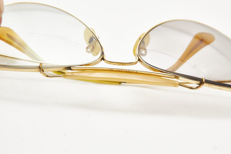 Puede incluir: Primer plano de gafas vintage con montura dorada y lentes transparentes. Las patillas son de color &aacute;mbar claro y la montura tiene un dise&ntilde;o delicado y cl&aacute;sico. El texto "MADE IN MANILA" es visible en la patilla.