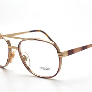May include: Aviator-style eyeglasses featuring a gold-tone metal frame with a double bridge design. The temples and frame edges display a brown tortoiseshell pattern. The right lens is etched with the brand name FILOS in a serif font.