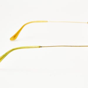 Puede incluir: Gafas de sol de aviador con montura dorada y lentes transparentes. Las patillas son finas y doradas, con una transici&oacute;n a un tono amarillo-verdoso en los terminales. Las lentes son de color gris claro y las almohadillas nasales son doradas.