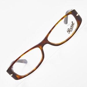 Puede incluir: Gafas marrones de carey con montura rectangular. El logotipo de Persol es visible en la lente. Las gafas tienen un diseño clásico y son adecuadas para el uso diario.