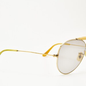 Puede incluir: Gafas de sol de aviador con montura dorada y lentes grises. Las gafas tienen doble puente y puntas de patillas amarillas. Las lentes tienen forma de l&aacute;grima. La montura es de color dorado brillante.